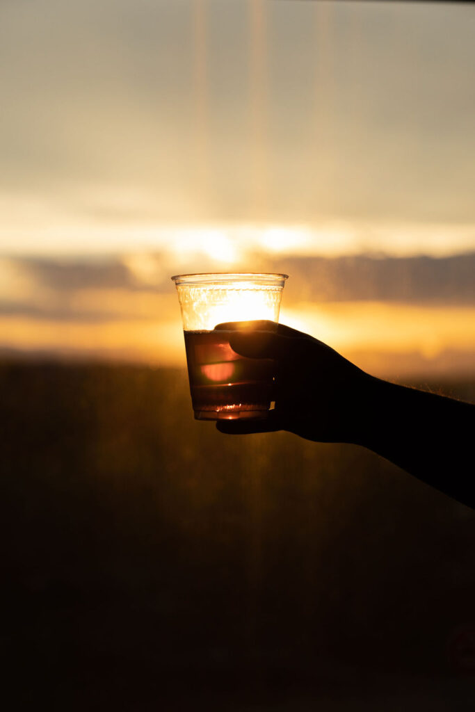 A beer held in the air at sunset